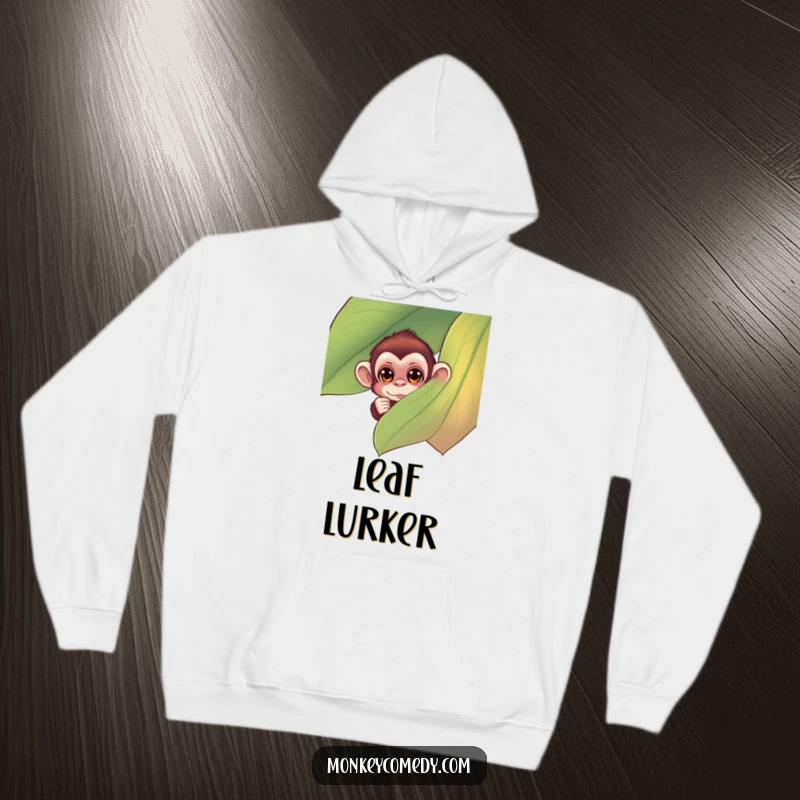 Funny monkey hoodie depicting a small monkey with curious eyes peeking from behind a large, colorful leaf, designed for warmth and humor.